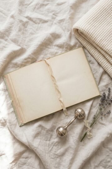 Open baby name book with blank pages beside a silver rattle, dried lavender and a folded cream blanket
