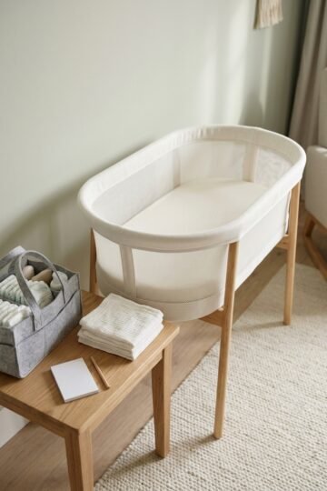 Empty white bassinet with a fitted sheet beside a diaper caddy and folded muslin cloths in soft daylight