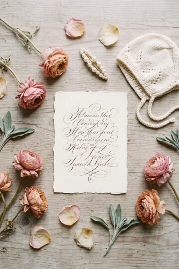 Cream card with handwritten names beside dried pink flowers, a knit bonnet and a pearl hair clip